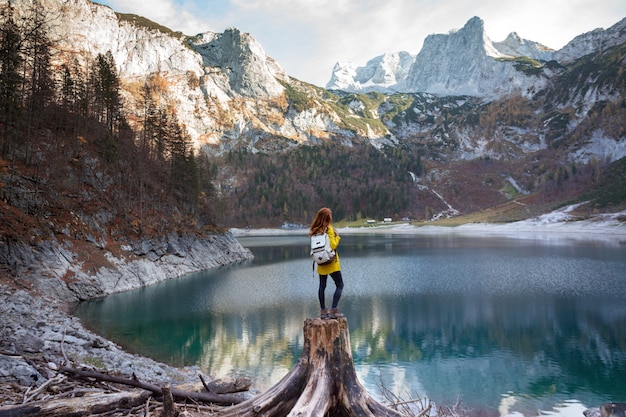 Girl with a backpack stands on the shore of a mountain lake