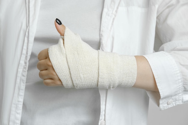 A girl with a bandaged hand shows a thumbs up a hand injury an elastic bandage first aid to the p