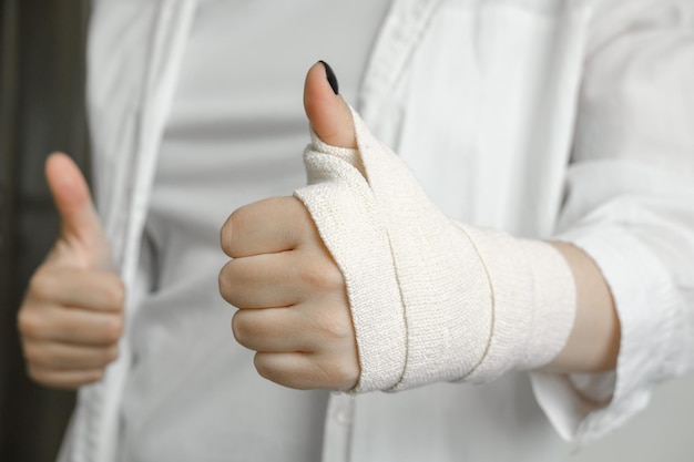 A girl with a bandaged hand shows a thumbs up a hand injury an elastic bandage first aid to the p