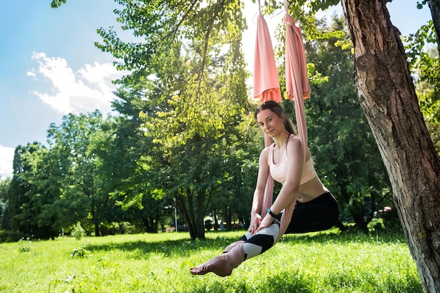 Girl with a beautiful fit pumped figure in a sports suit for yoga stretches in the air near a tree The concept of aerial paintings in the open air