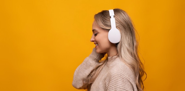 A girl with big headphones listens to her favorite music on a yellow background