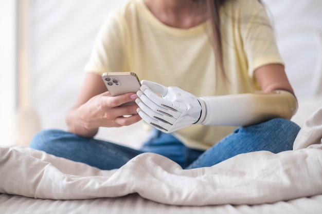 Girl with bionic arm using phone reading social media and chatting in bed woman with disability learning or working online remotely from home