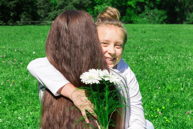 A girl with blond hair combed in a bun gives her mother a bouquet of white flowers