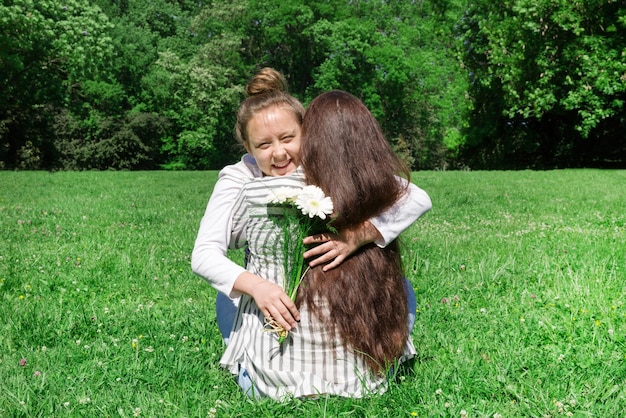 A girl with blond hair combed in a bun gives her mother a bouquet of white flowers