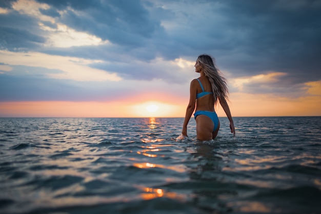 Girl with blond hair in a swimsuit posing against the backdrop of the sunset in the estuary enjoying nature around him