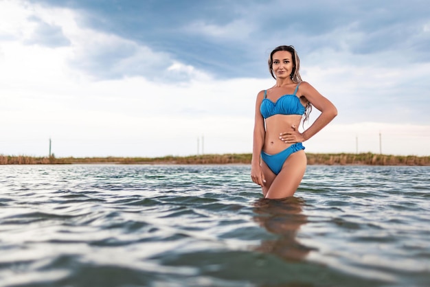 Girl with blond hair in a swimsuit posing against the backdrop of the sunset in the estuary enjoying nature around him