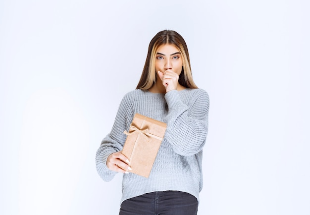 Girl with a cardboard gift box looks confused and thrilled.