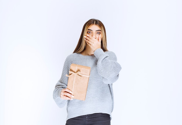 Girl with a cardboard gift box looks confused and thrilled.