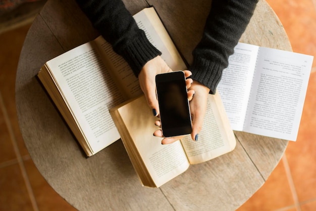 Girl with cell phone and books on a wooden table