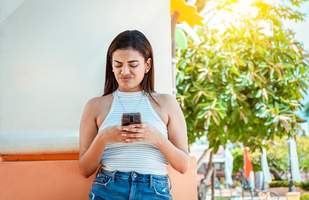 Girl with the cell phone receiving an unpleasant message Young woman with cell phone reading a message with an unpleasant face Upset girl frowning reading unpleasant message