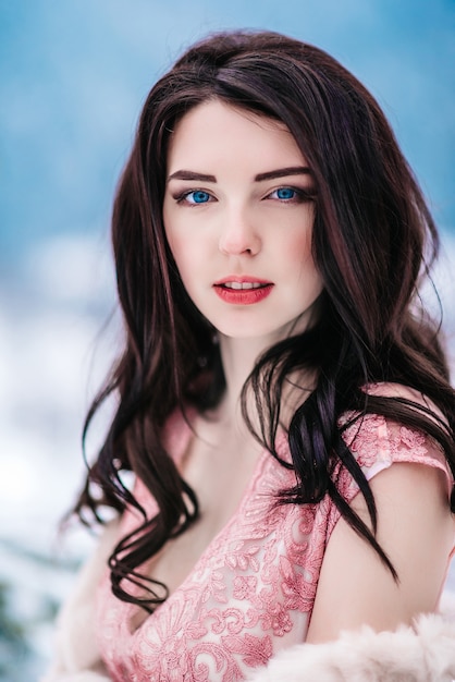 Girl with chestnut hair, blue eyes and a pink dress on the background of the winter mountains