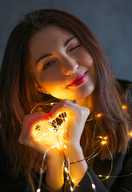 A girl with a Christmas garland. Light in hands, in the form of a heart