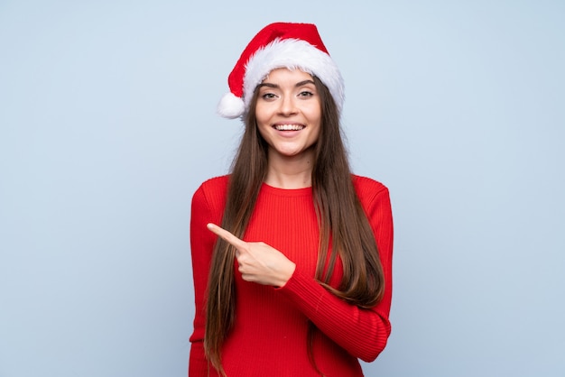 Girl with christmas hat over isolated blue pointing finger to the side