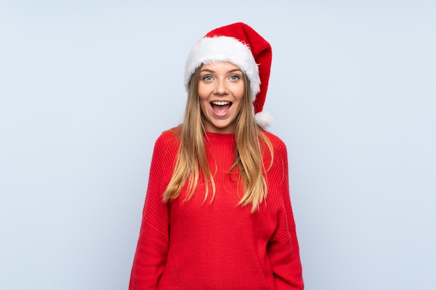 Girl with christmas hat over isolated blue wall with surprise facial expression