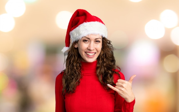 Girl with christmas hat making phone gesture over unfocused wall