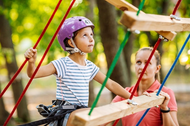 Girl with climbing gear in an adventure park are engaged in rock climbing or pass obstacles on the rope road