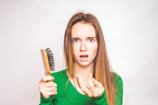 Girl with a comb and problem hair isolated on white. Holds sick hair in hand