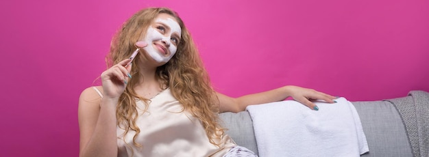 A girl with a cosmetic mask on her face sits on the sofa