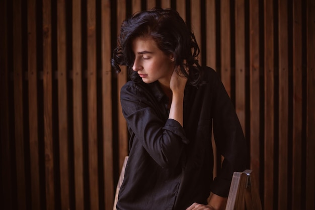 Girl with curly dark hair and natural makeup sitting on a leather chair vintage photo processing