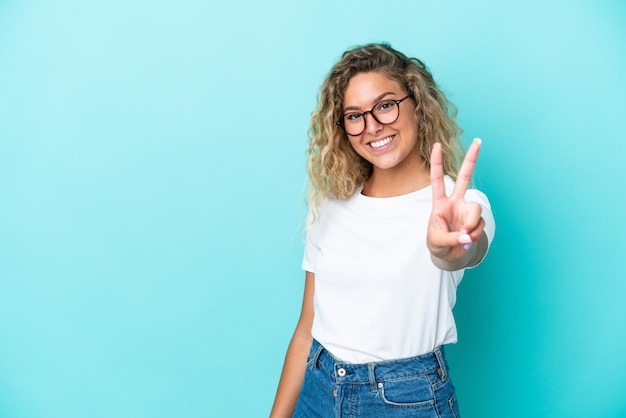 Girl with curly hair isolated on blue background smiling and showing victory sign