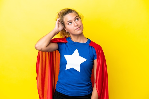 Girl with curly hair isolated on yellow background in superhero costume and having doubts