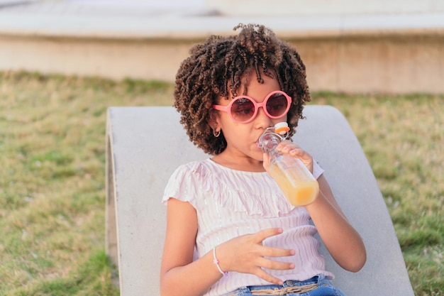 Girl with curly hair sitting on a park bench drinking juice