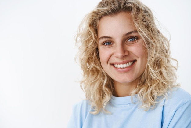 Girl with cute sincere smile laughing and having fun looking friendly and delighted at camera with deep blue eyes standing happily over white background in tshirt giggling flirty