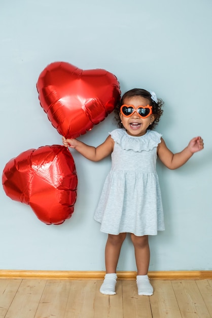 girl with dark, black skin color, celebrate valentine's day. heart shaped red foil balloons and glasses.