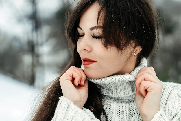 Girl with dark hair posing in a snowy forest.