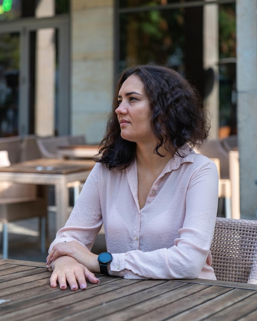 A girl with dark hair sits in a street cafe and looks thoughtfully into the distance