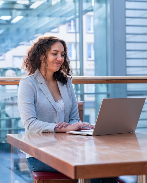 A girl with dark hair works at a table with a laptop Behind a large window