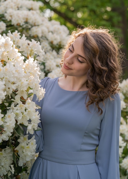 girl with dark wavy hair in a gray dress tenderly looks at white flowers of rhododendrons