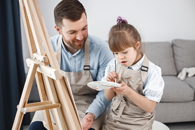 Girl with Down syndrome and her father painting on an easel with brushes