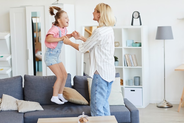 Girl with down syndrome jumping on the sofa she playing with her mother while they are at home