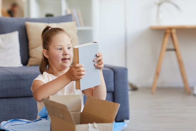 Girl with down syndrome taking the book out of the box while sitting in the room