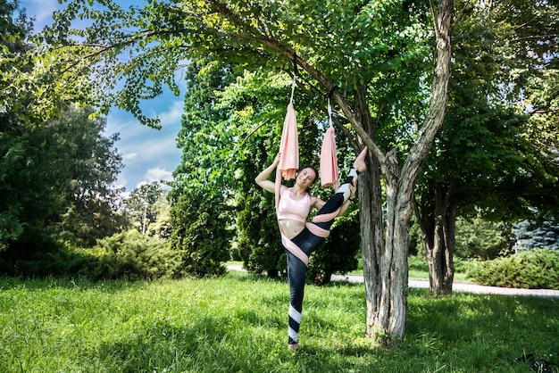 Girl with a fit pumped figure in a sports suit for yoga stretches in the air near a tree