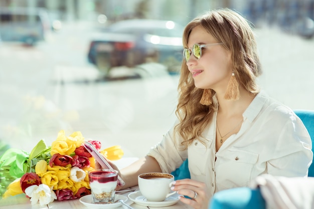 Girl with flowers, coffee, yogurt, and phone in a cafe