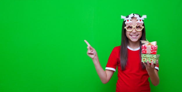 Girl with funny glasses hold gifts for christmas new year in her hands pointing to advertising space