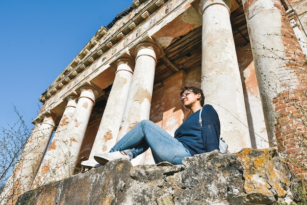 Girl with glasses sits against the background of an abandoned building an abandoned church