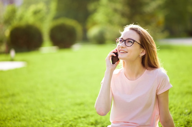 Girl with glasses talking on the phone outdoors. copy space.