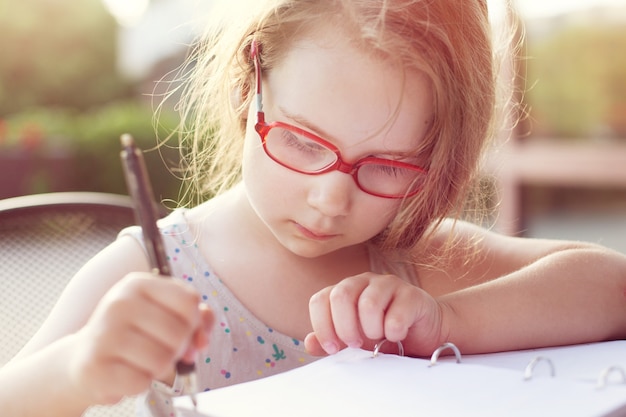 Girl with glasses writes in a notebook. sunny soft background. doing homework outdoors