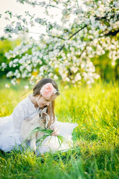 Girl with a goat sitting in the grass in a lush apple orchard