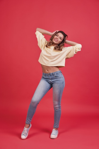 Girl with a great style.   Full length of beautiful young woman smiling and looking at camera while standing against pink background