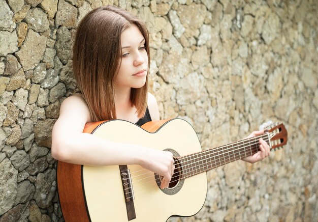 girl with a guitar against a brown wall