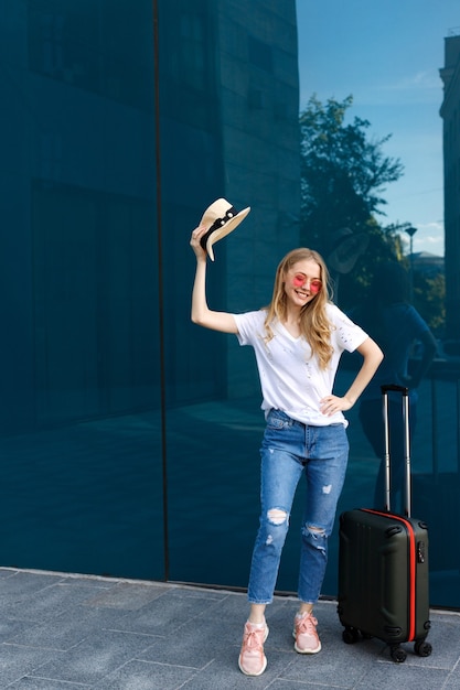 Girl with hat and luggage on a blue background happy and travels