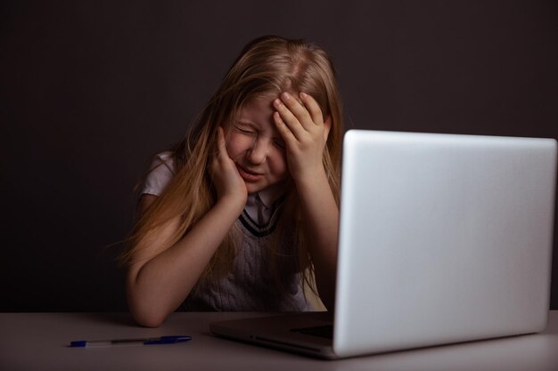 Girl with headache sitting at the desk and doing homework isolated Tired child using computer