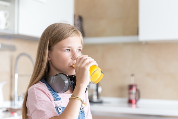 Girl with headphones drinking orange juice in the kitchen