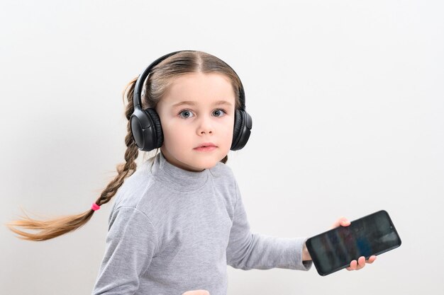 A girl with headphones and a phone on a white background a girl with pigtails listens to music in headphones photo with copy space