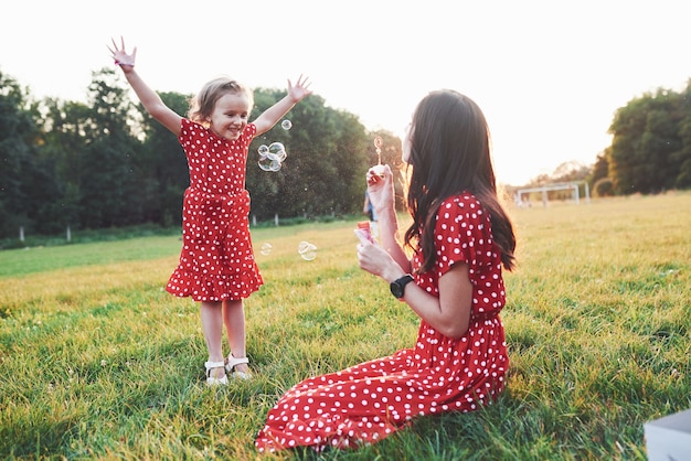 Girl with her daughter having fun with bubbles outside sitting on the grass