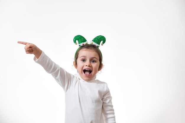 The girl with the hoop in the form of an elf hat on her head points her finger to the side.